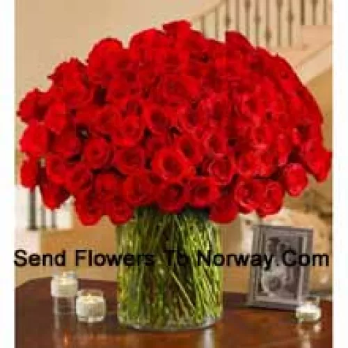 101 roses rouges avec quelques fougères dans un grand vase en verre